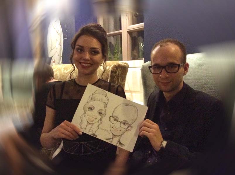 жена с улыбкой и муж в очках позируют шаржисту на свадьбе в кафе Чехов Шарж в Минске и Калининграде